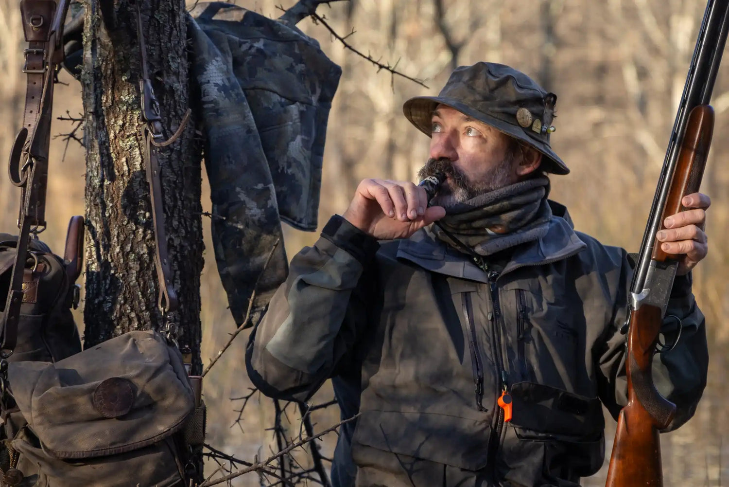 A man in hunting attire holding a shotgun and a vape.