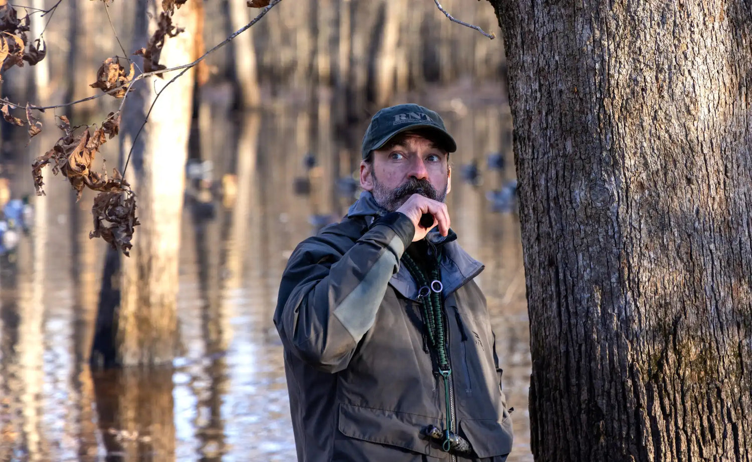 A man in a camouflage jacket and hat blowing a duck call.