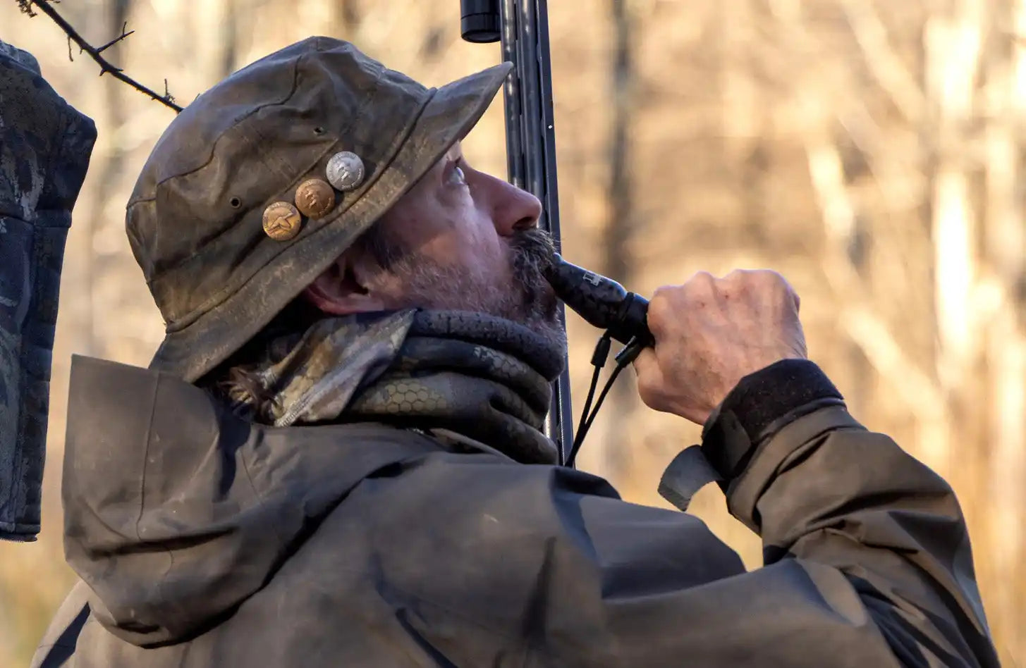A man wearing a hat and jacket, using a game call.