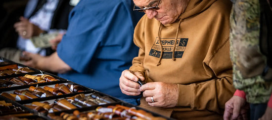 A man wearing a tan hoodie with ’joseph’s’ printed on the chest is examining wooden-handled tools arranged in black trays.